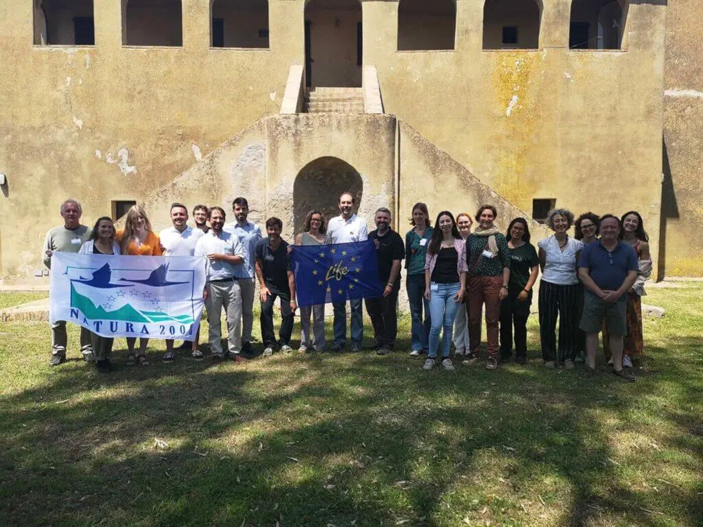 Group of people with a banner on a lawn in front of a historic building