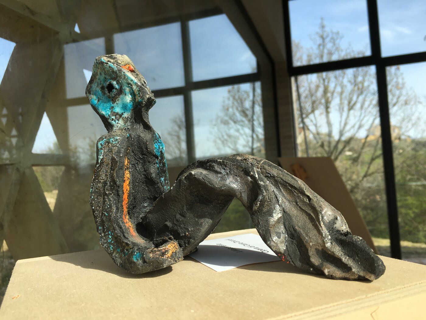 Colourful sculpture of a reclining figure in front of a large window